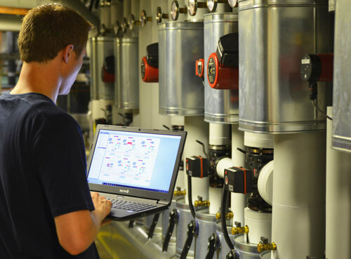 Mitarbeiter mit Laptop bei den Pumpen einer Heizungsanlage