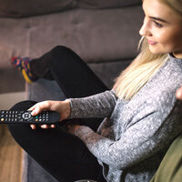 Eine Frau mit einer TV-Fernbedienung auf der Couch